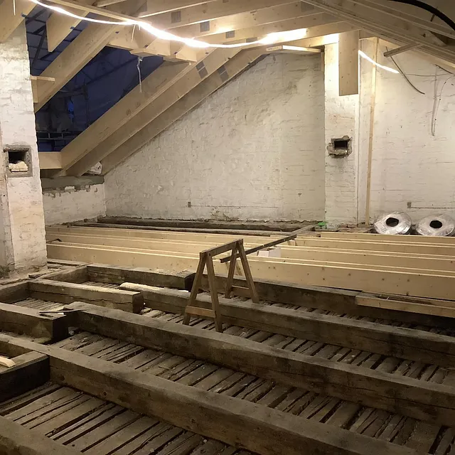 Loft under renovering med nye trebjelker og synlige murvegger.