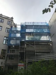 Byggefasade med stillas dekket av blått nett under renovering.