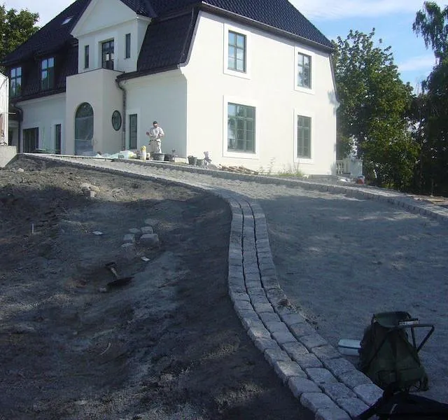 Nyoppusset hvitt hus med svart tak, og en steinlagt sti under arbeid i hagen.