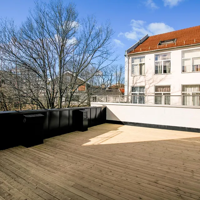 Stor takterrasse med tregulv, svarte rekkverk og utsikt mot nabolaget.