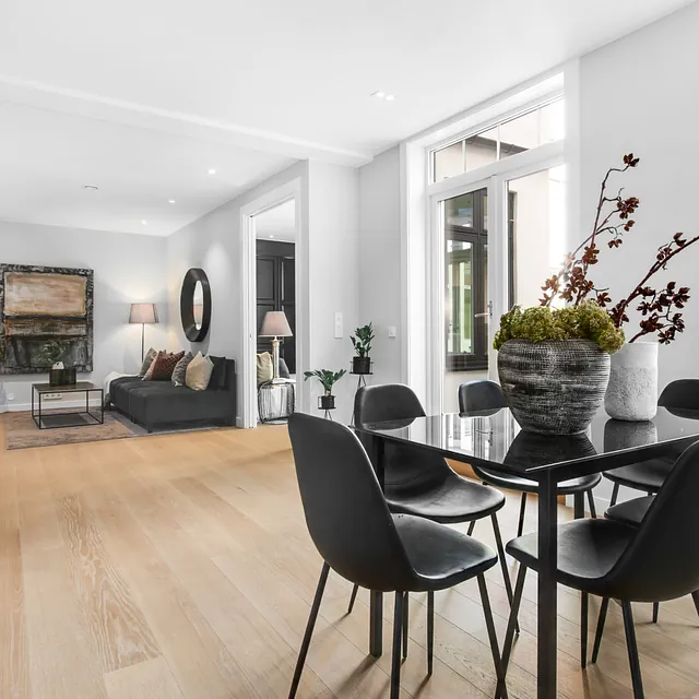 Moderne og lys stue med åpen løsning til spisestue. Svarte møbler, grønne planter og store vinduer gir et stilrent preg.