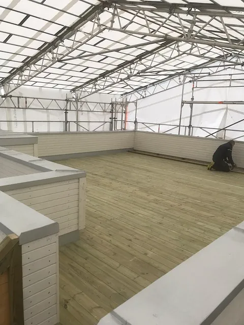 Stor takterrasse med lyse tregulv og hvite rekkverk under teltdekke.