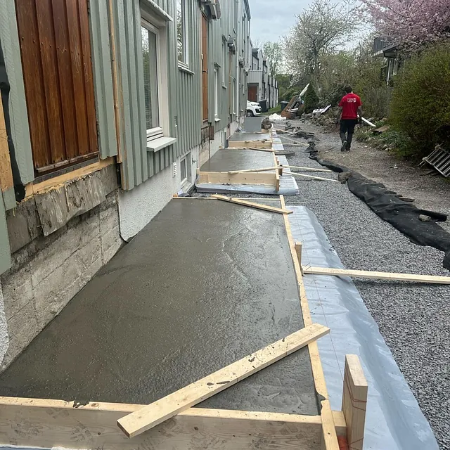 Nylig støpt betongfundament langs rekkehusfasade.